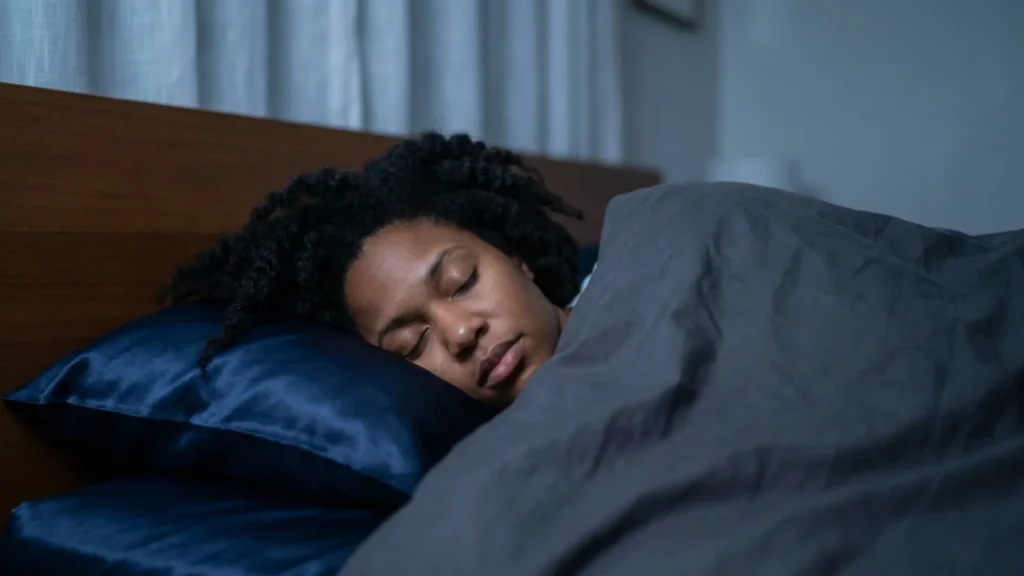 Woman sleeping peacefully on a jewel-toned satin pillowcase with natural hair spread across it