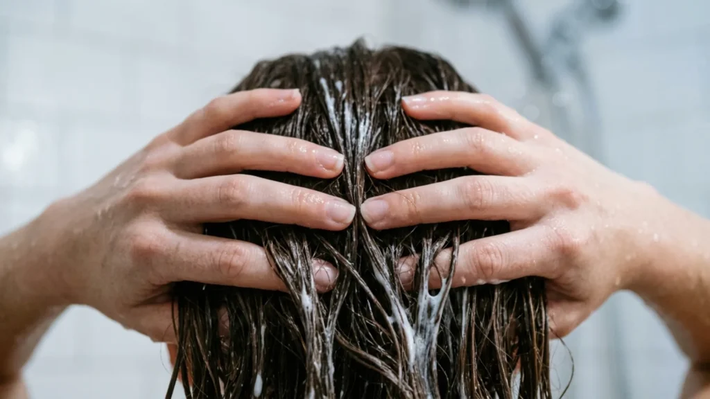 Hands working a hair mask through the mid-length to ends of damp hair