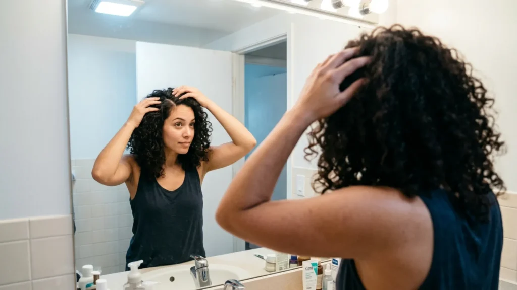 Woman parting her hair to check her scalp's oil level in the mirror