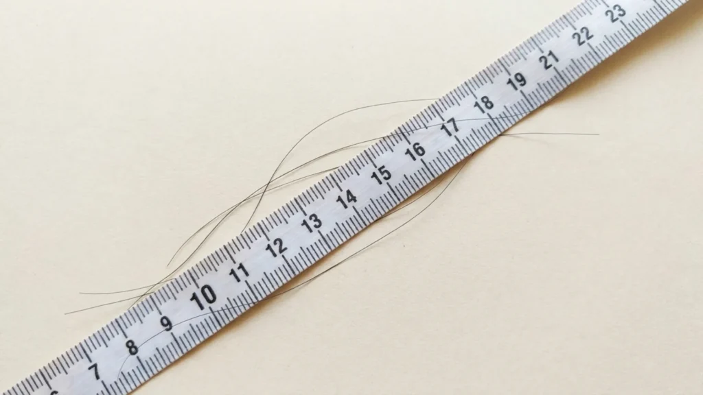 Measuring tape held against a hair strand to track hair growth rate
